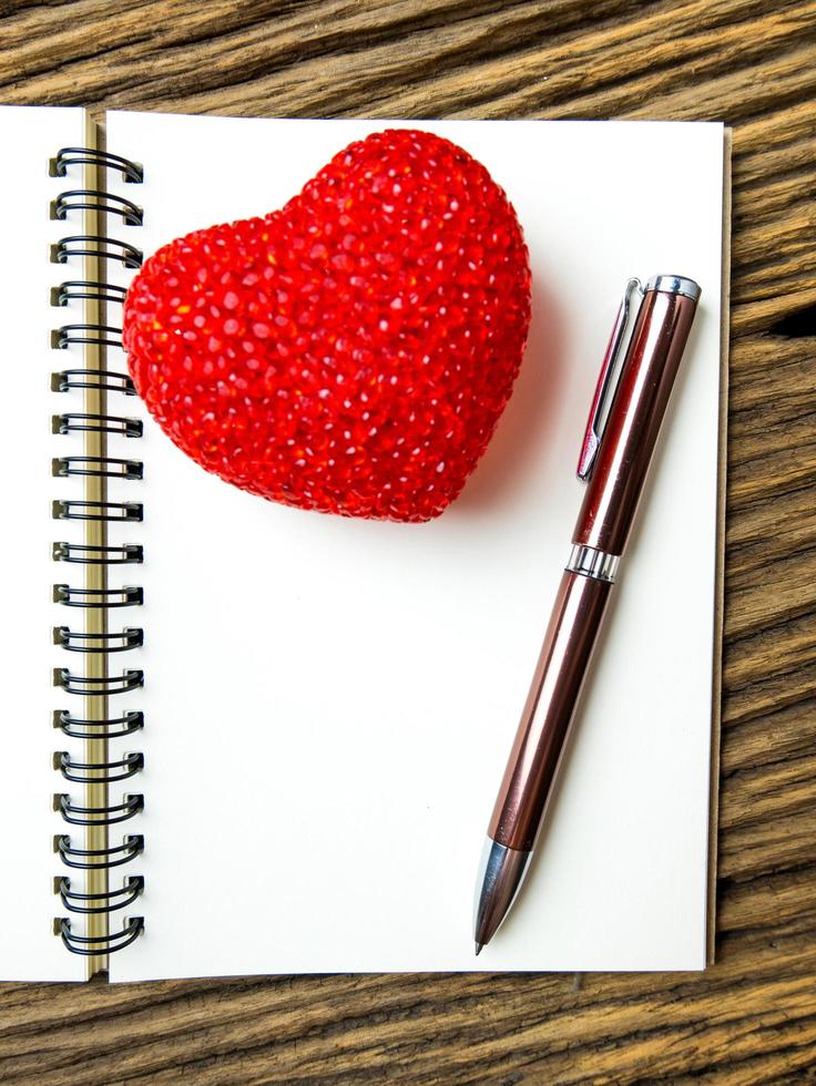 Draufsicht auf Notizbuch und Stift mit rotem Herzen auf Holzschwarzgrund, Valentinstag foto