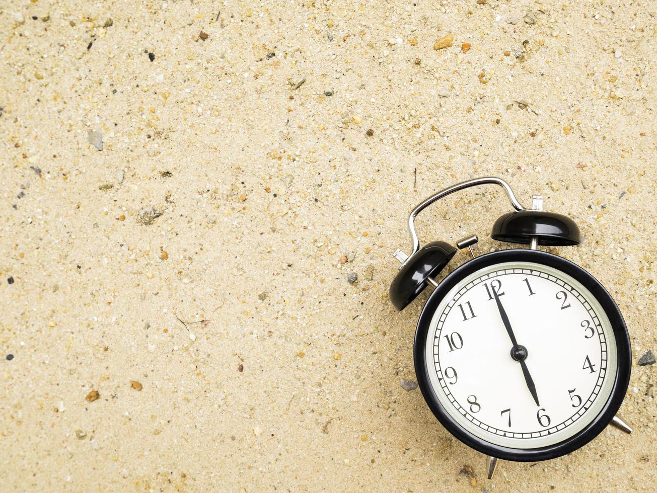 Wecker auf Strandsand, der sechs Uhr anzeigt foto