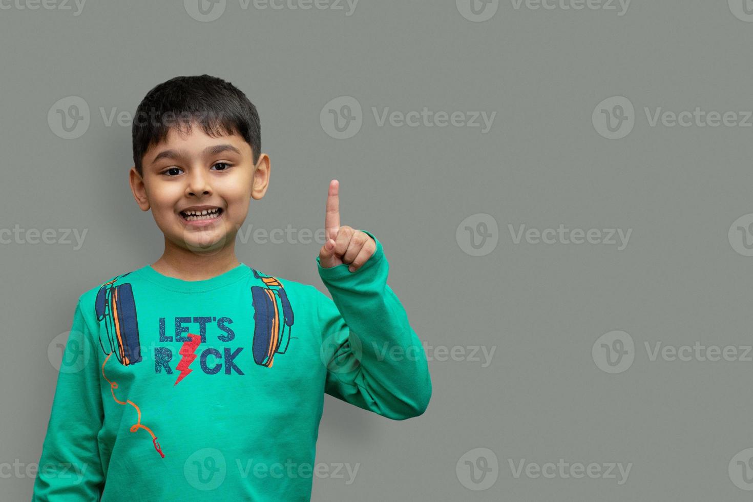 lächelnder glücklicher Junge, der mit dem Finger auf den Kopierraum zeigt, der über einfarbigem Hintergrund isoliert ist? foto