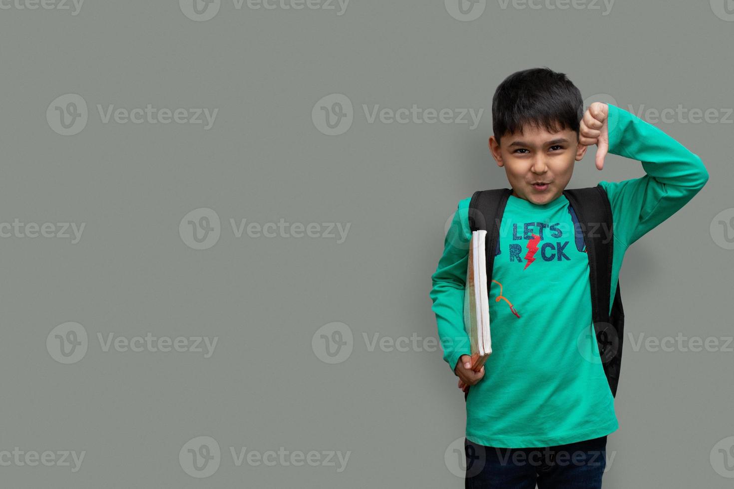 Trauriger Kinderjunge mit Büchern in der Hand und Tasche auf den Schultern, Hassstudienkonzept Kopienraum foto