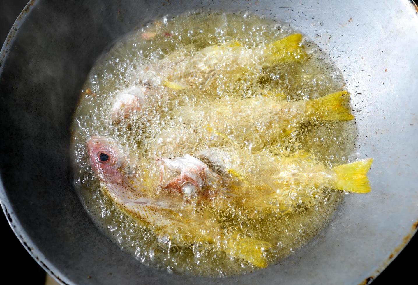Braten von Fisch in Speiseöl mit Eisenpfanne. foto