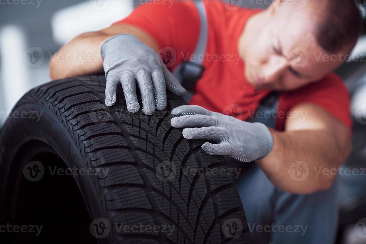 Mechaniker, der einen Reifen in der Werkstatt hält. Wechsel von Winter- und Sommerreifen foto