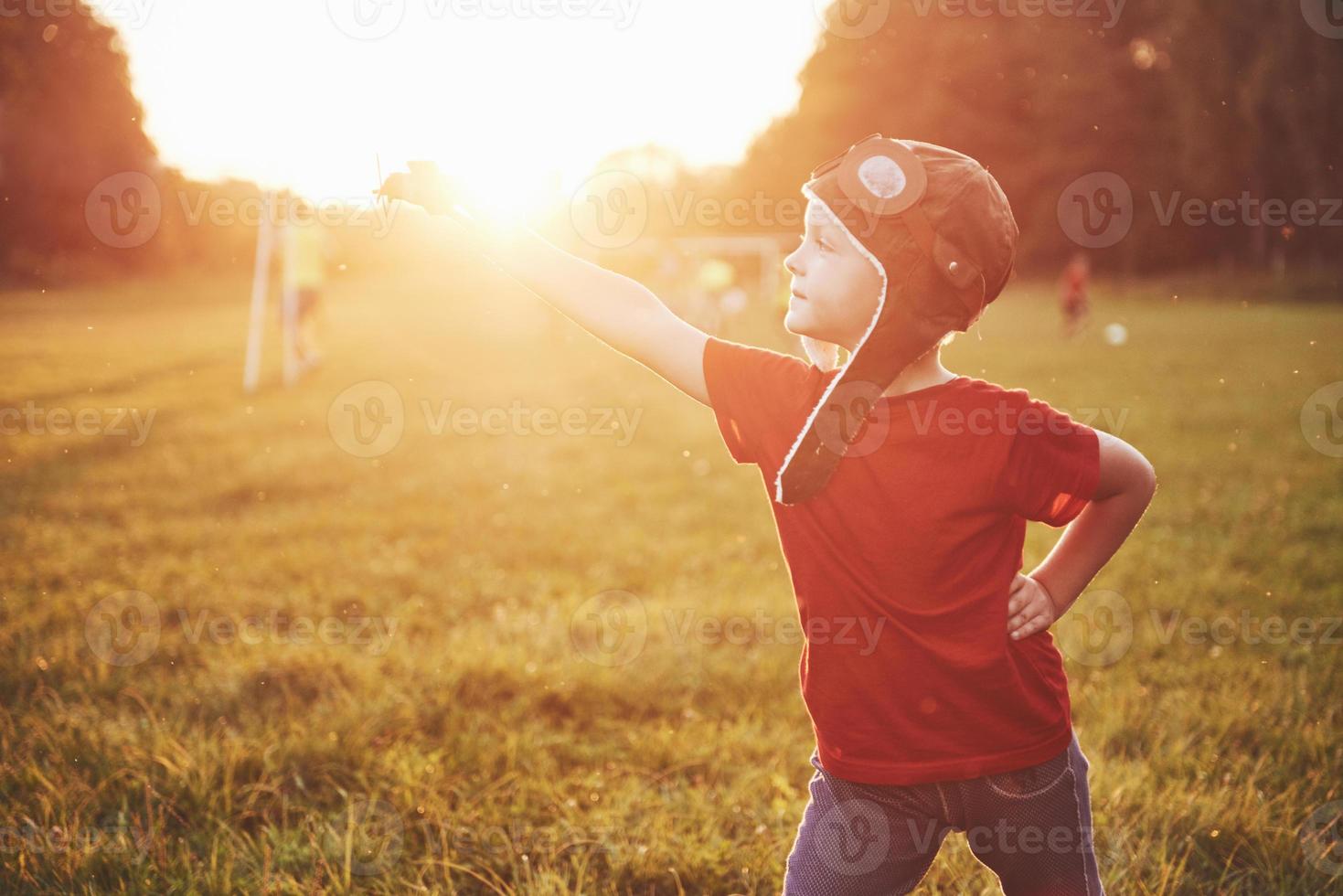 glückliches Kind im Pilotenhelm, das mit einem hölzernen Spielzeugflugzeug spielt und davon träumt, fliegen zu werden foto