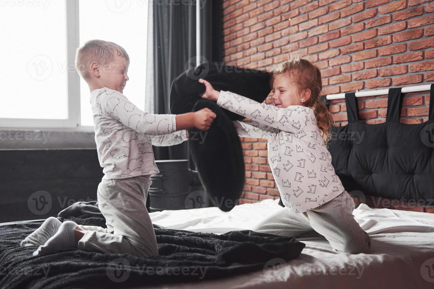 ungezogene kinder kleine junge und mädchen inszenierten eine kissenschlacht auf dem bett im schlafzimmer. sie mögen solche spiele foto