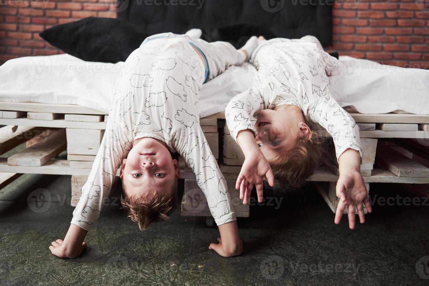 glückliche Kinder, die im schwarzen Schlafzimmer spielen. kleiner Junge und Mädchen, Bruder und Schwester spielen im Schlafanzug auf dem Bett foto