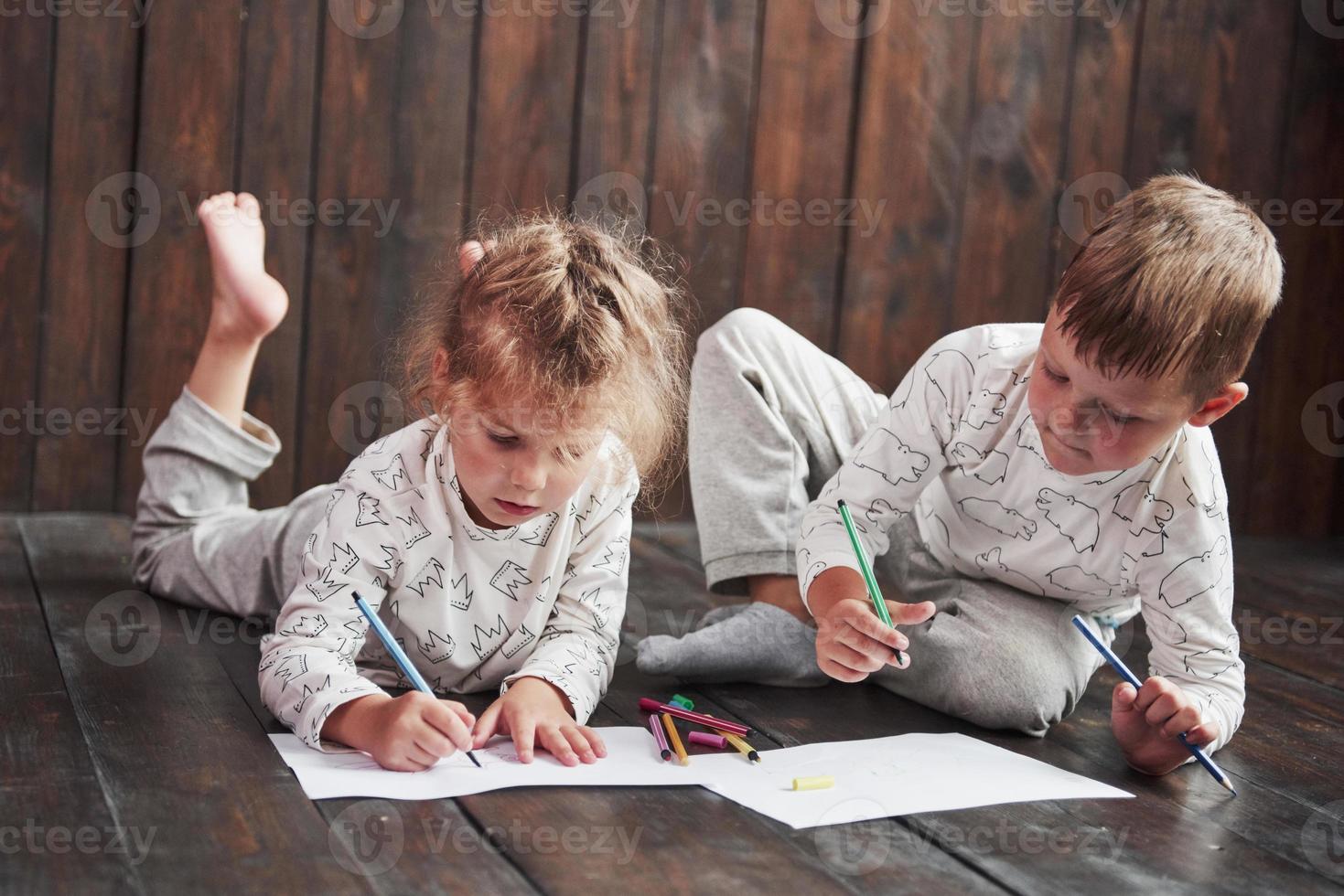 Kinder liegen im Schlafanzug auf dem Boden und zeichnen mit Bleistiften. süßes Kind malen mit Bleistiften foto
