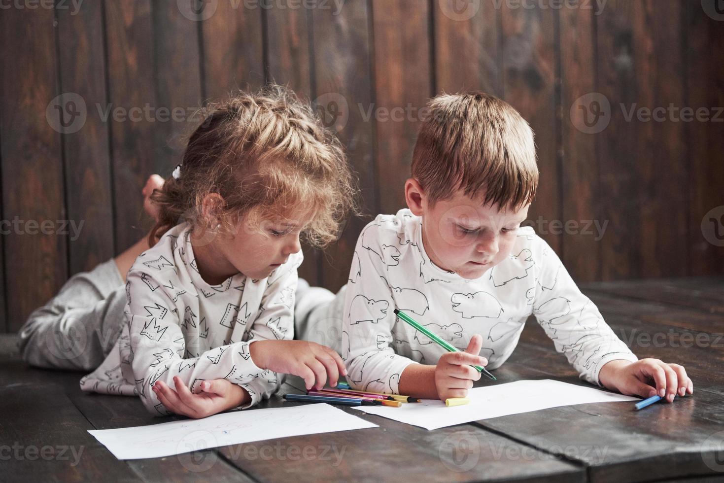 Kinder liegen im Schlafanzug auf dem Boden und zeichnen mit Bleistiften. süßes Kind malen mit Bleistiften foto