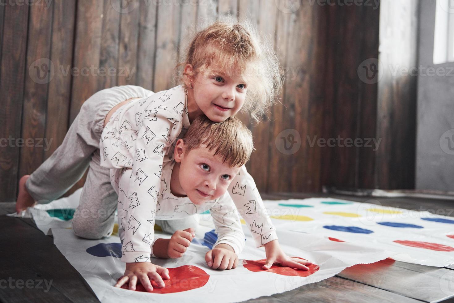 zwei glückliche Kinder spielen im Twister im Haus. Bruder und Schwester haben eine lustige Zeit im Urlaub foto