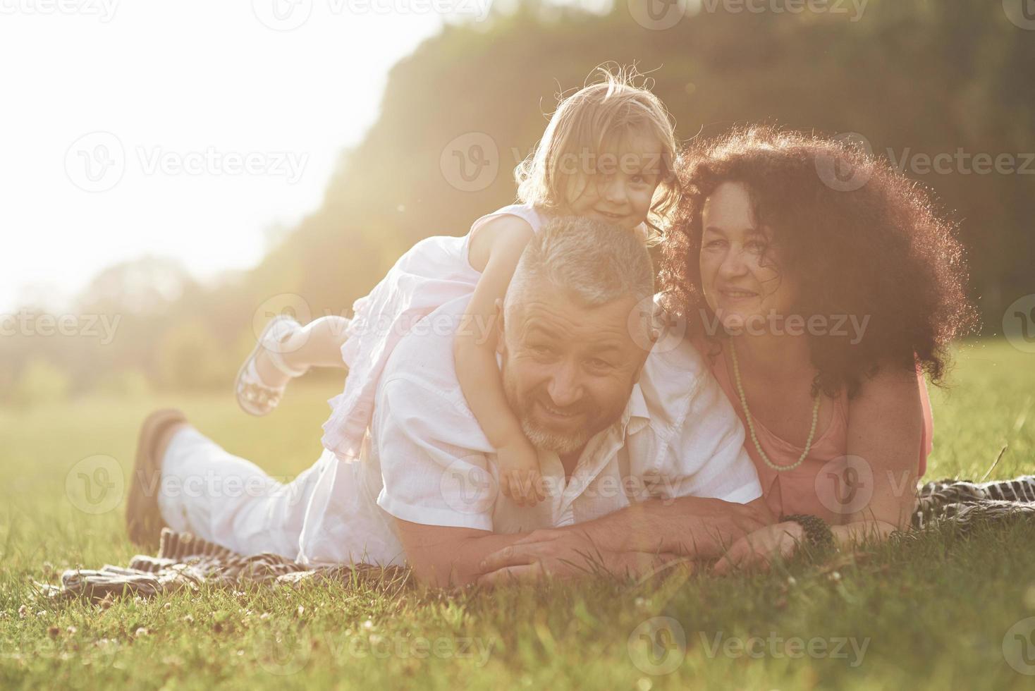 Ein süßes kleines Mädchen verbringt Zeit mit ihrem geliebten Großvater und ihrer geliebten Großmutter im Park. sie machten ein Picknick im Gras foto