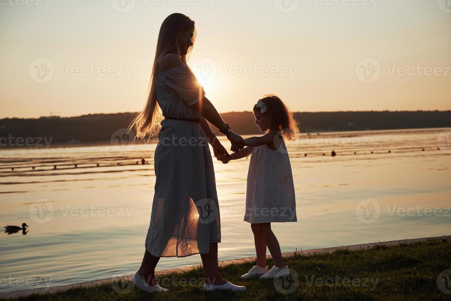 Mama spielt mit ihrem Baby im Urlaub am Meer, Silhouetten bei Sonnenuntergang foto