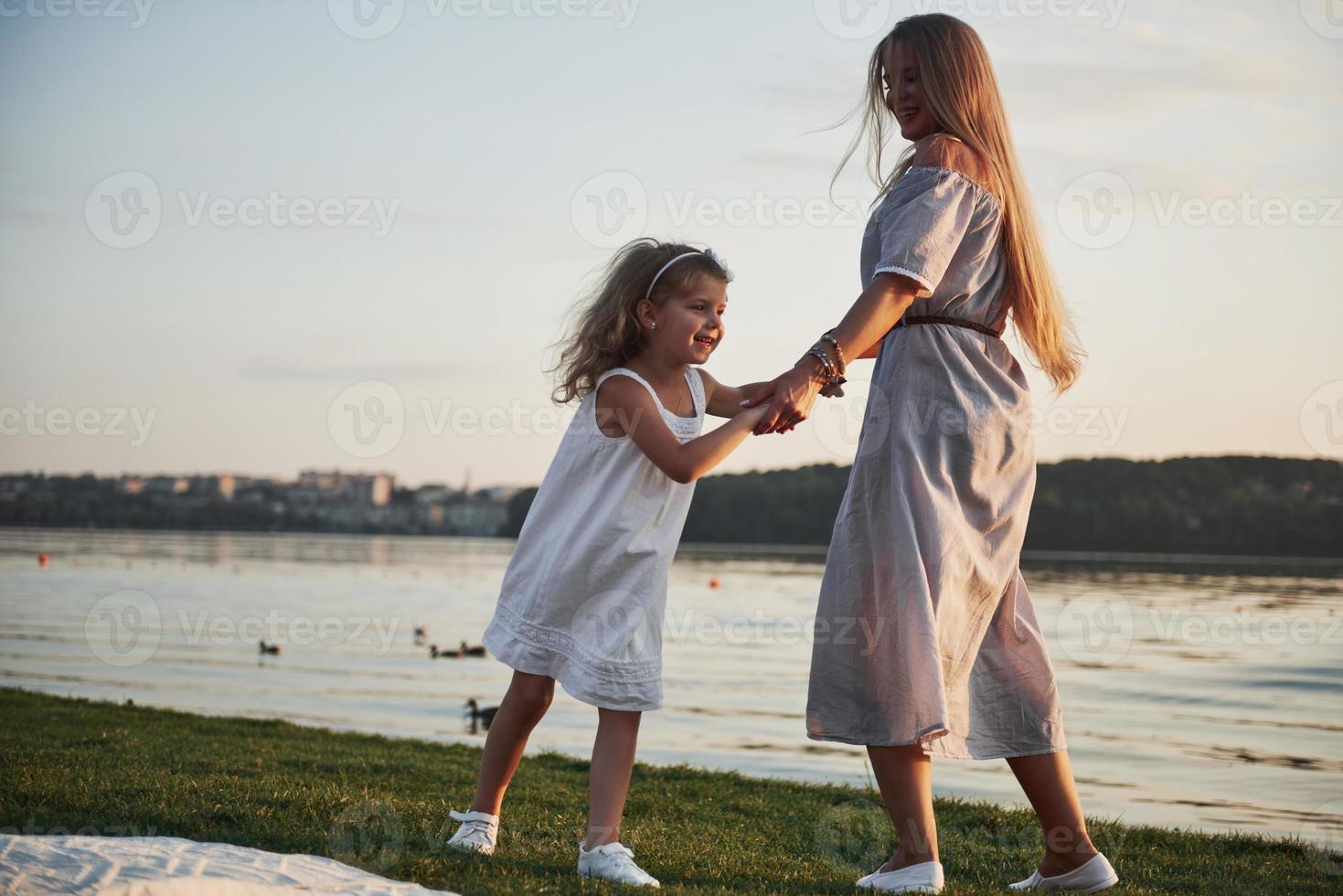 Mama und ihre kleine Tochter spielen auf dem Gras in der Nähe des Sees. foto