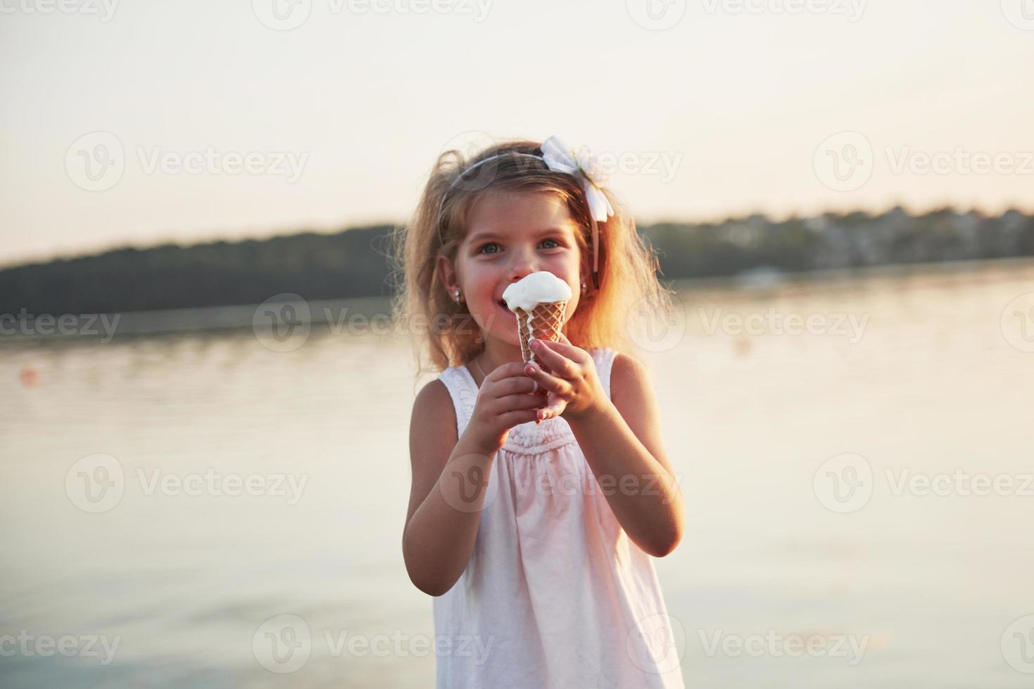 Ein hübsches kleines Mädchen isst ein Eis in der Nähe des Wassers foto