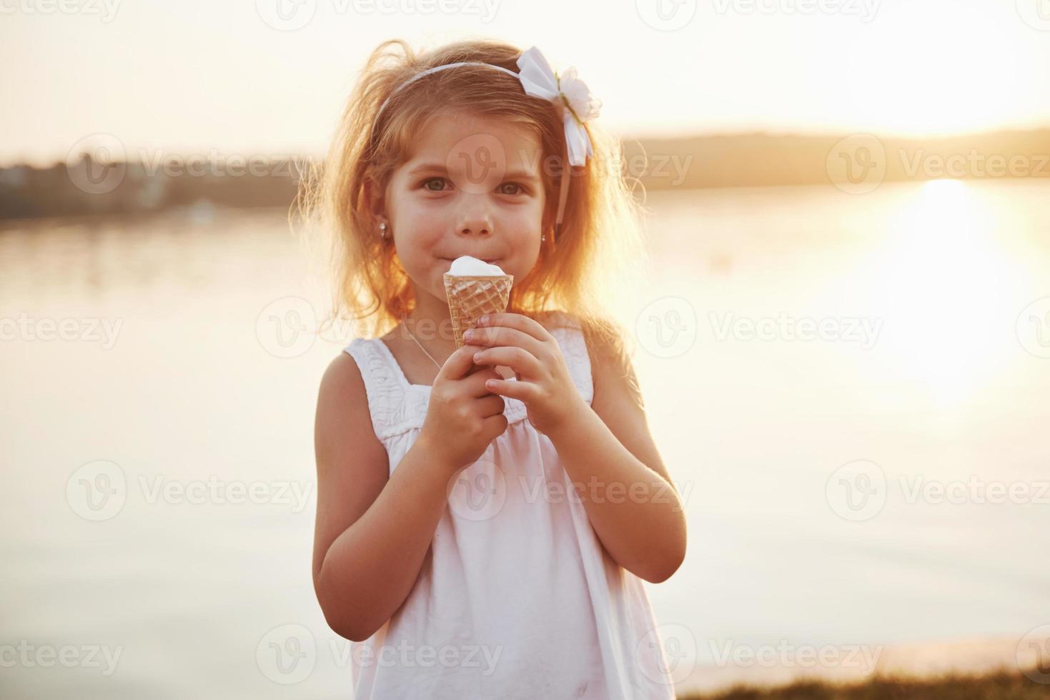 Ein hübsches kleines Mädchen isst ein Eis in der Nähe des Wassers foto