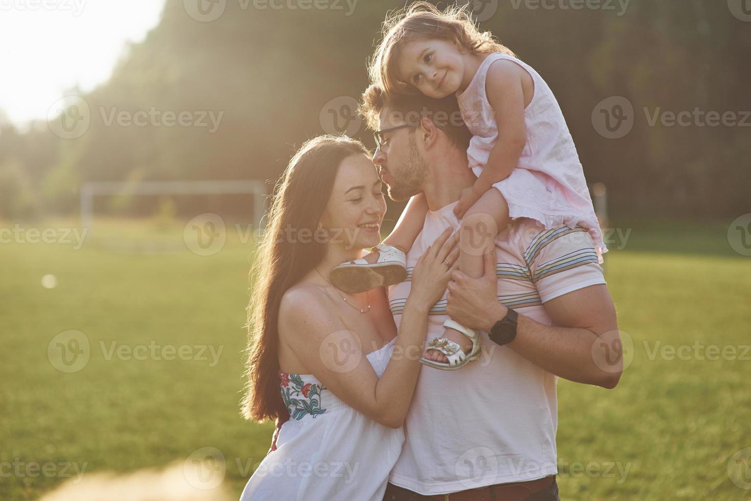 Mutter und Vater verbringen glücklich Zeit miteinander. kleine Tochter spielt bei Sonnenuntergang mit ihren Eltern im Freien foto