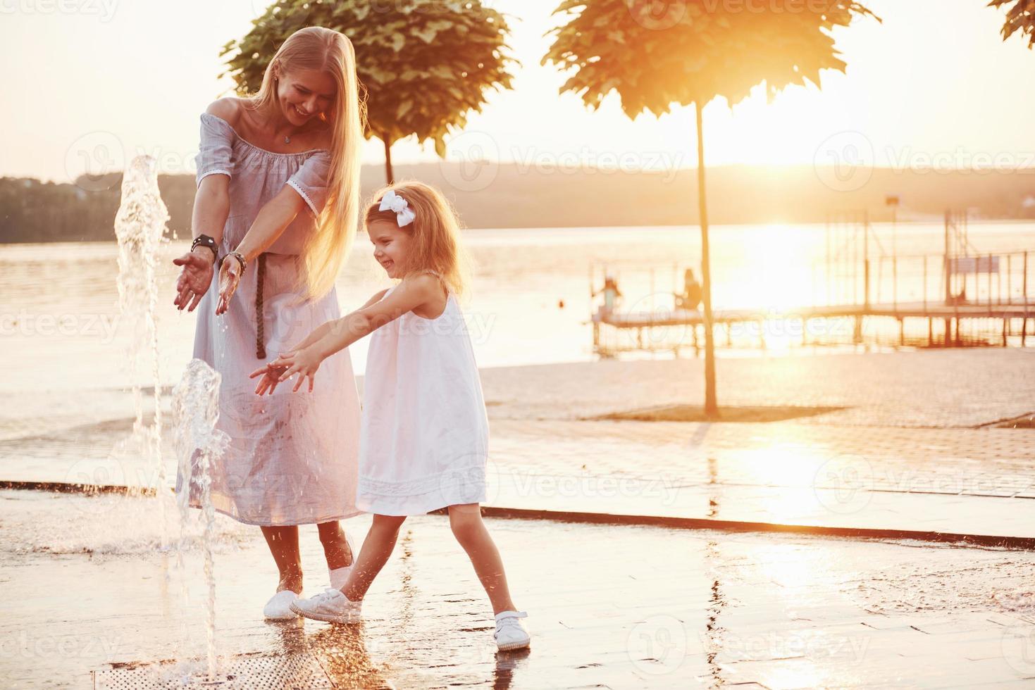 eine Frau, die bei Sonnenuntergang mit einem Kind am Meer im Park spielt foto