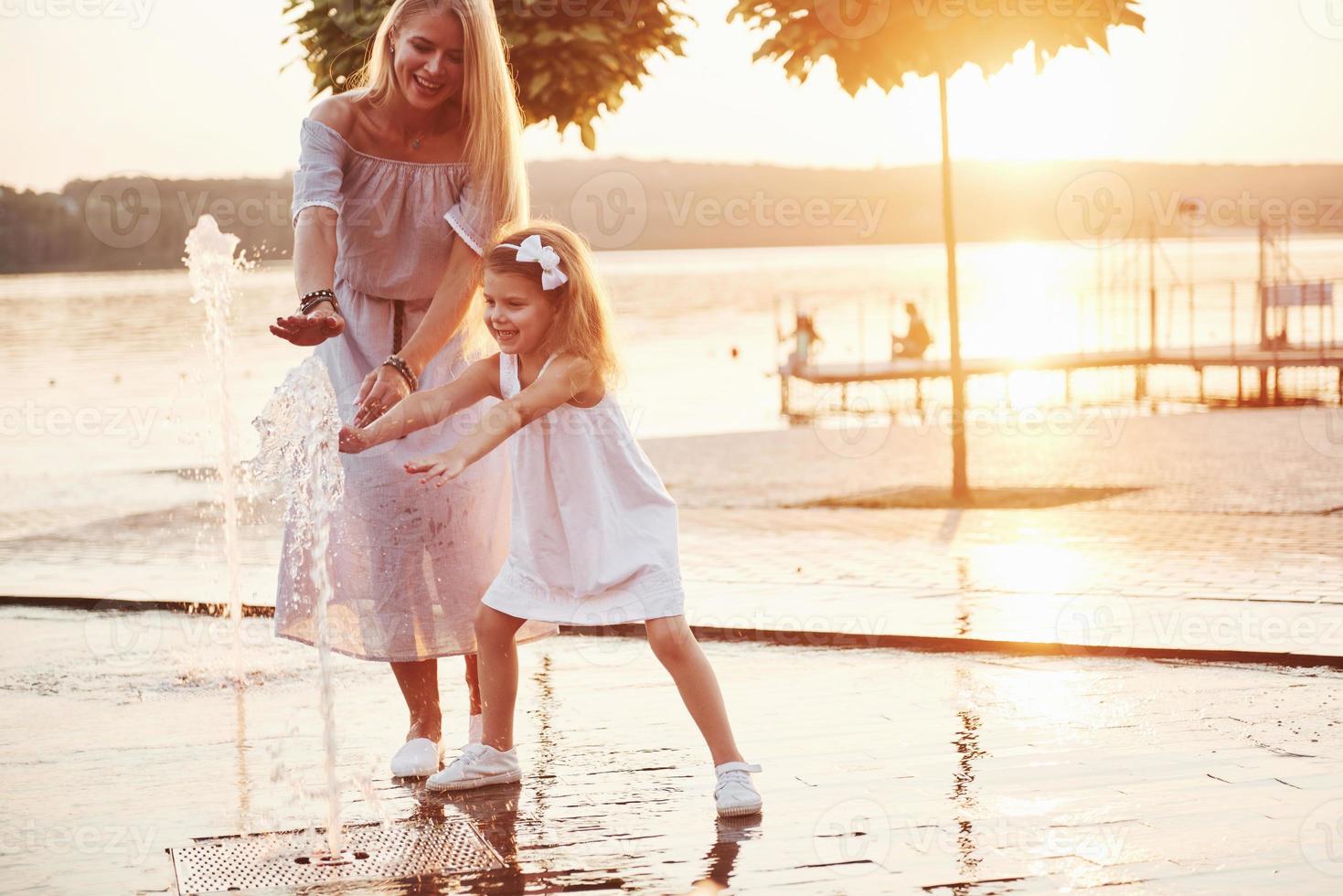 eine Frau, die bei Sonnenuntergang mit einem Kind am Meer im Park spielt foto