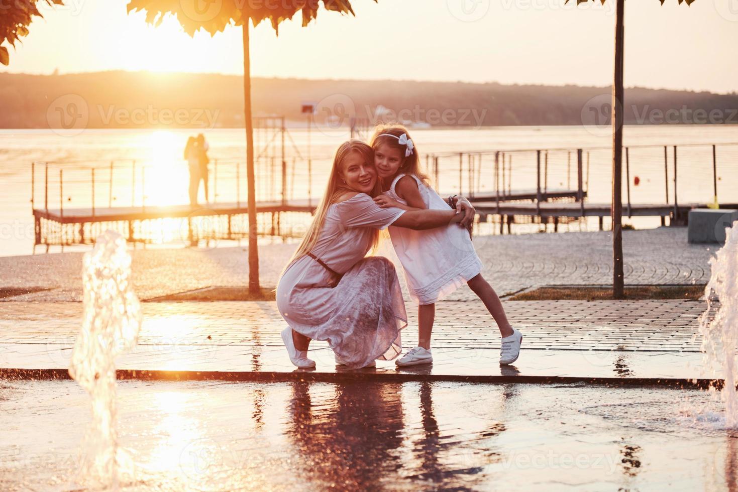 eine Frau, die bei Sonnenuntergang mit einem Kind am Meer im Park spielt foto