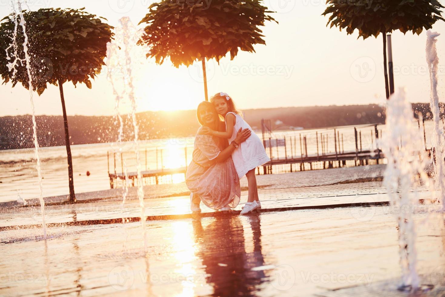 Mutter mit Baby in der Nähe des Brunnens bei Sonnenuntergang foto