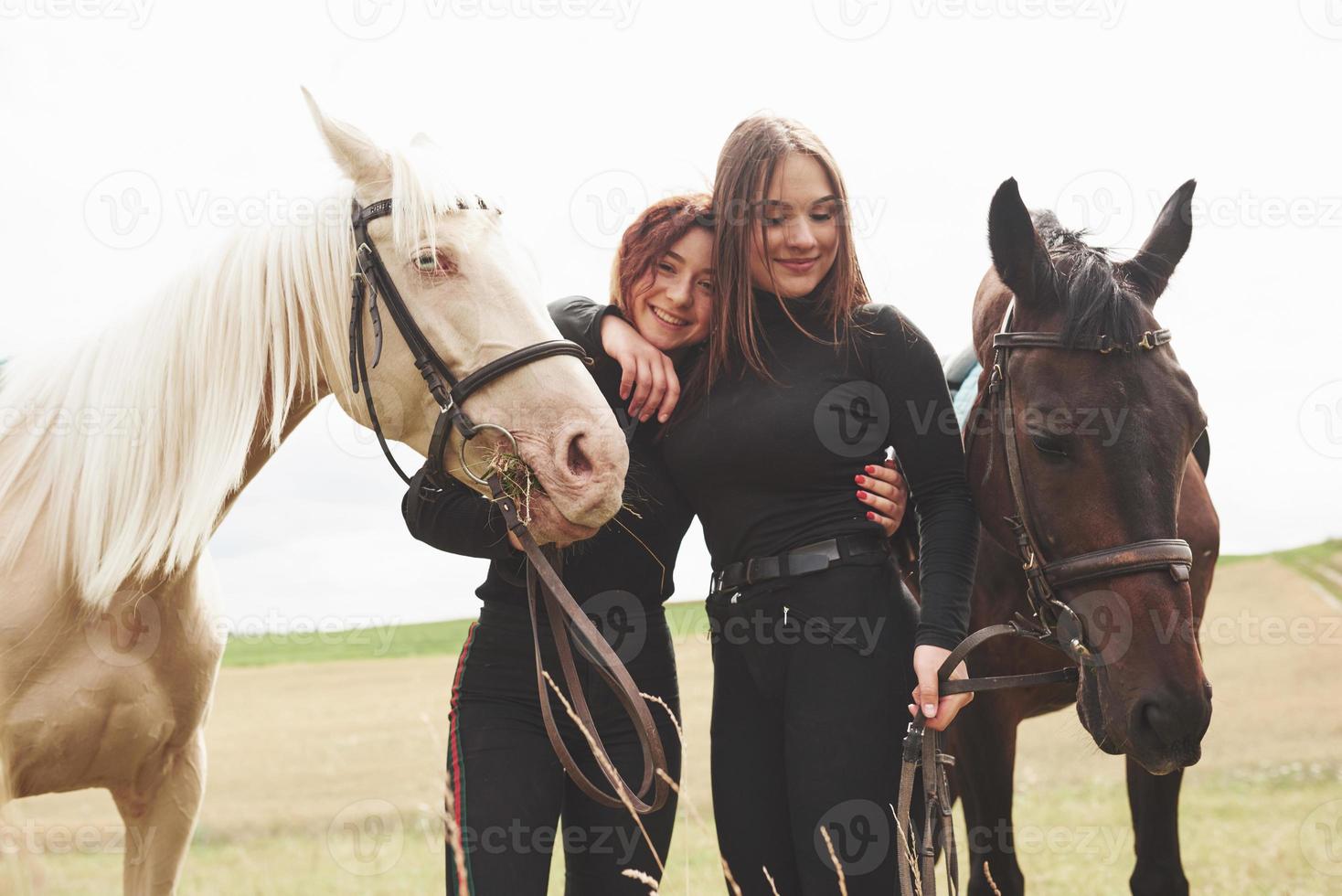 zwei junge schöne mädchen in ausrüstung zum reiten in der nähe ihrer pferde. sie lieben tiere foto