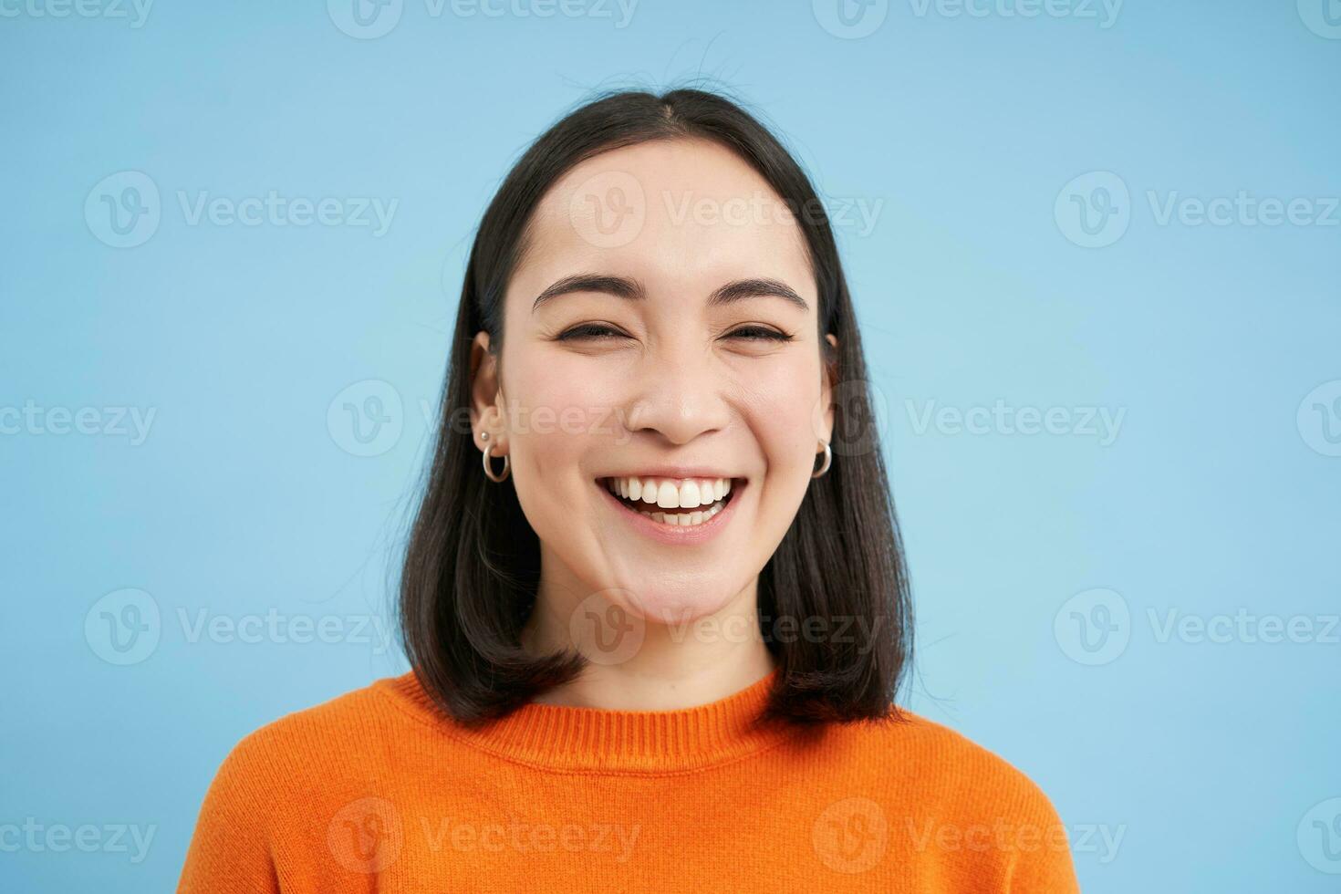 schließen oben Porträt von schön Lachen asiatisch Frau, zeigt an offen Glück, lächelnd beim Kamera, Stehen Über Blau Hintergrund foto