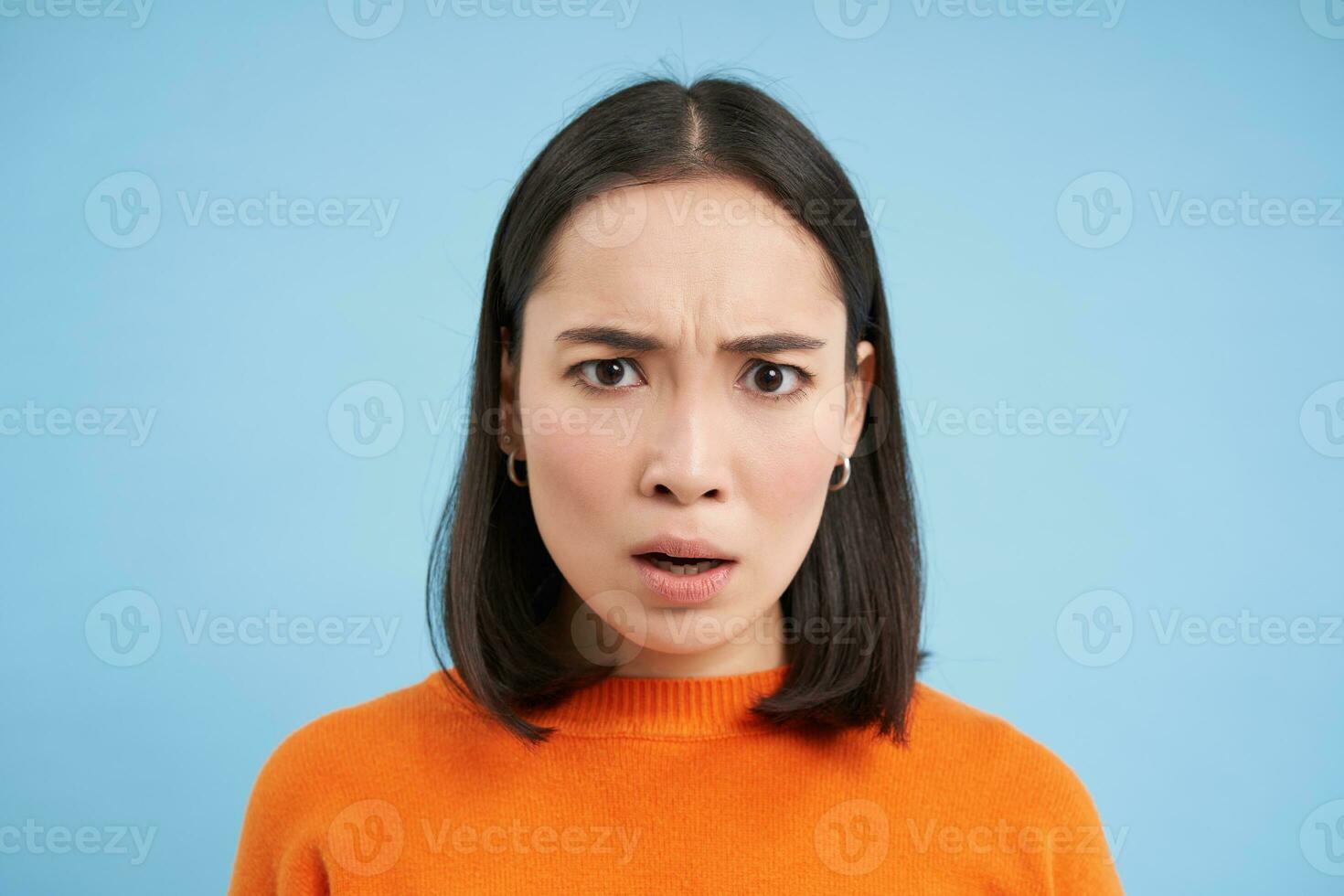 schließen oben Porträt von asiatisch Mädchen mit schockiert Gesicht, sieht aus beim etw unglaublich, erschrocken durch Nachricht, steht Über Blau Hintergrund foto