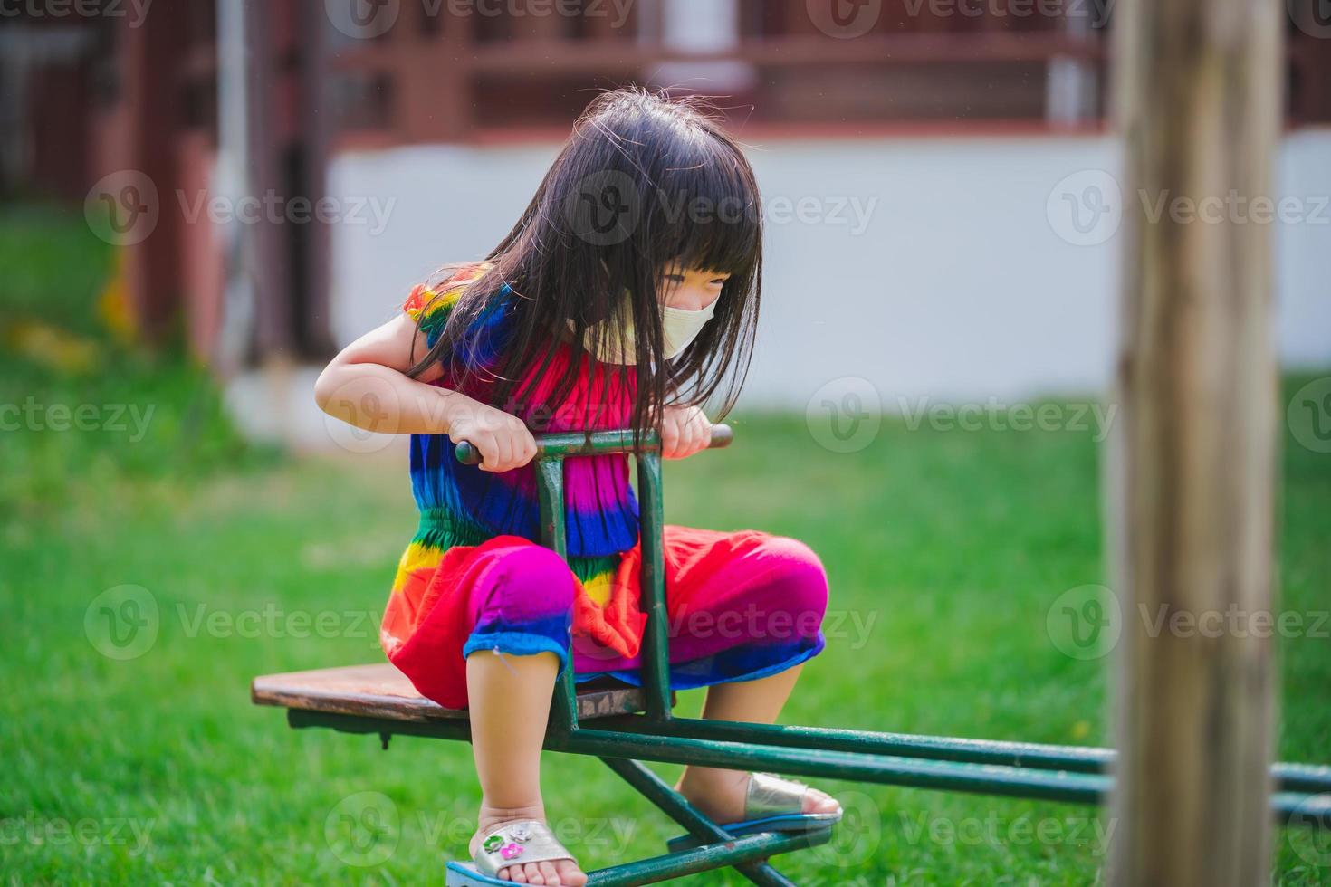 Kind mit Maske spielt mit niedergeschlagenem Pferd. Mädchen spielte Spielplatzgeräte. Verhindern Sie die Verbreitung von Coronavirus und PM2.5-Staub durch Luftverschmutzung. Kinder trainieren. entspannende Zeit für ein 4-jähriges Kind. foto