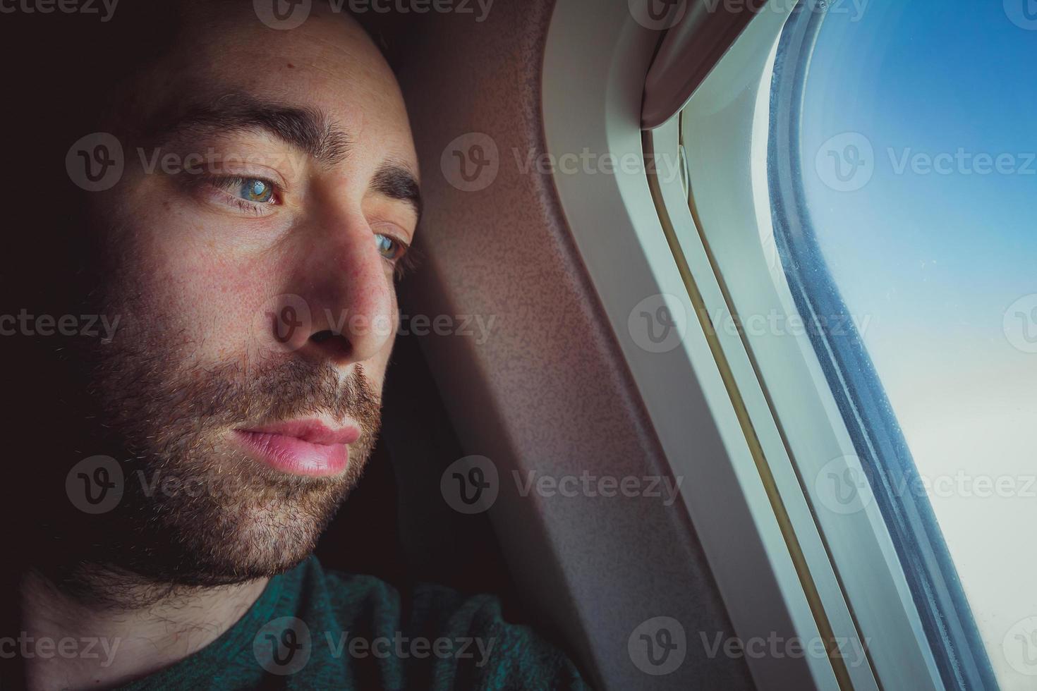 Nahaufnahme eines nachdenklichen Mannes, der durch das Fenster eines Flugzeugs nach draußen schaut foto