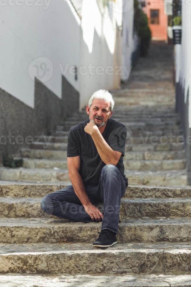 reifer Mann mit weißem Haar sitzt auf städtischen Stufen foto