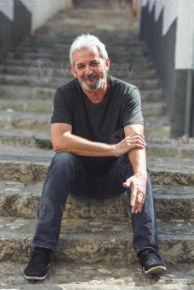 reifer Mann mit weißem Haar sitzt auf städtischen Stufen foto