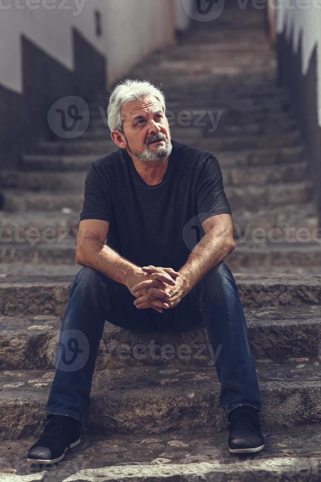 reifer Mann sitzt auf Stufen im städtischen Hintergrund foto