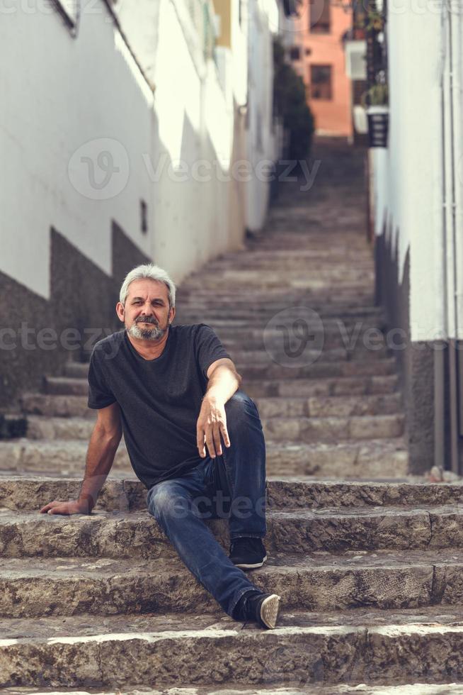 reifer Mann sitzt auf Stufen im städtischen Hintergrund foto