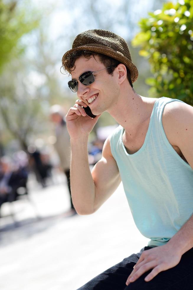 attraktiver junger Mann mit Hut, der auf dem Handy spricht foto