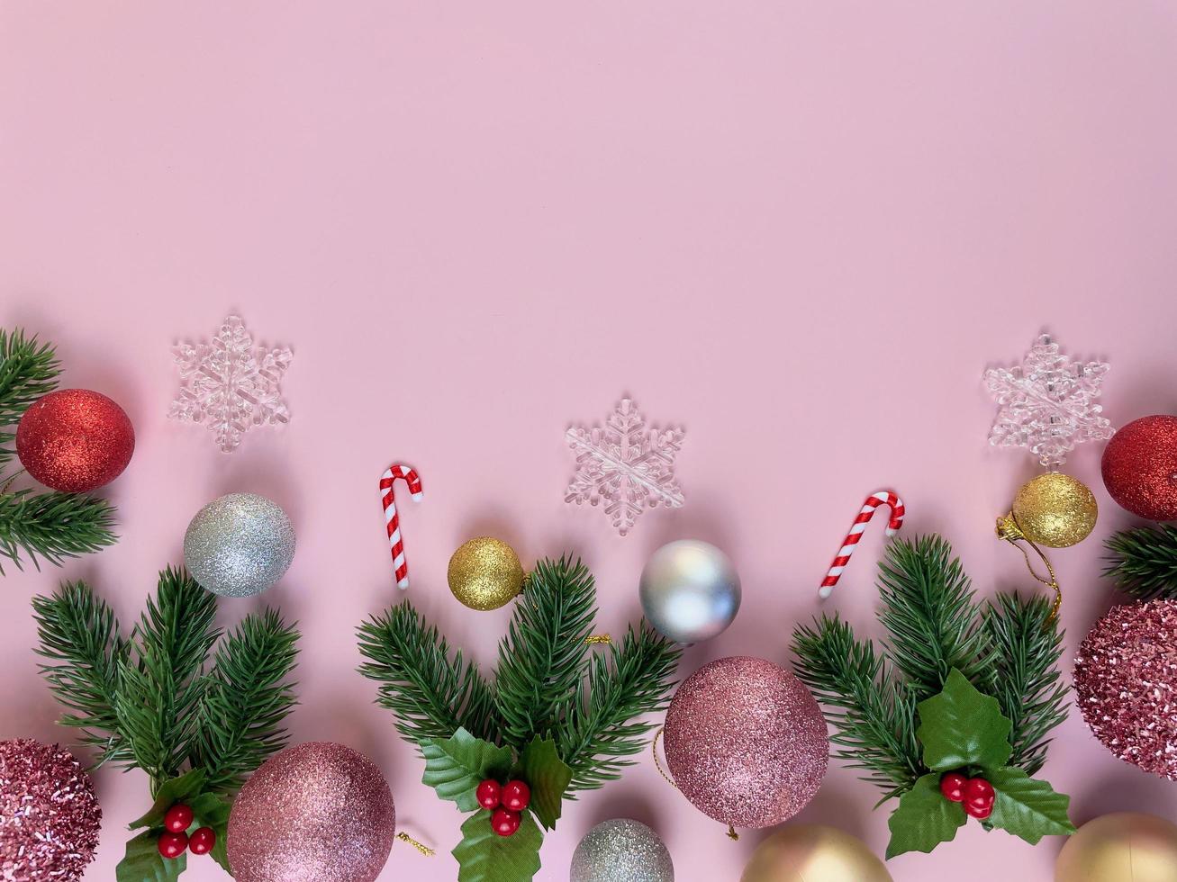 Weihnachtsschmuck, Kiefernblätter, goldene Kugeln, Schneeflocken, rote Kugeln auf rosa Hintergrund foto