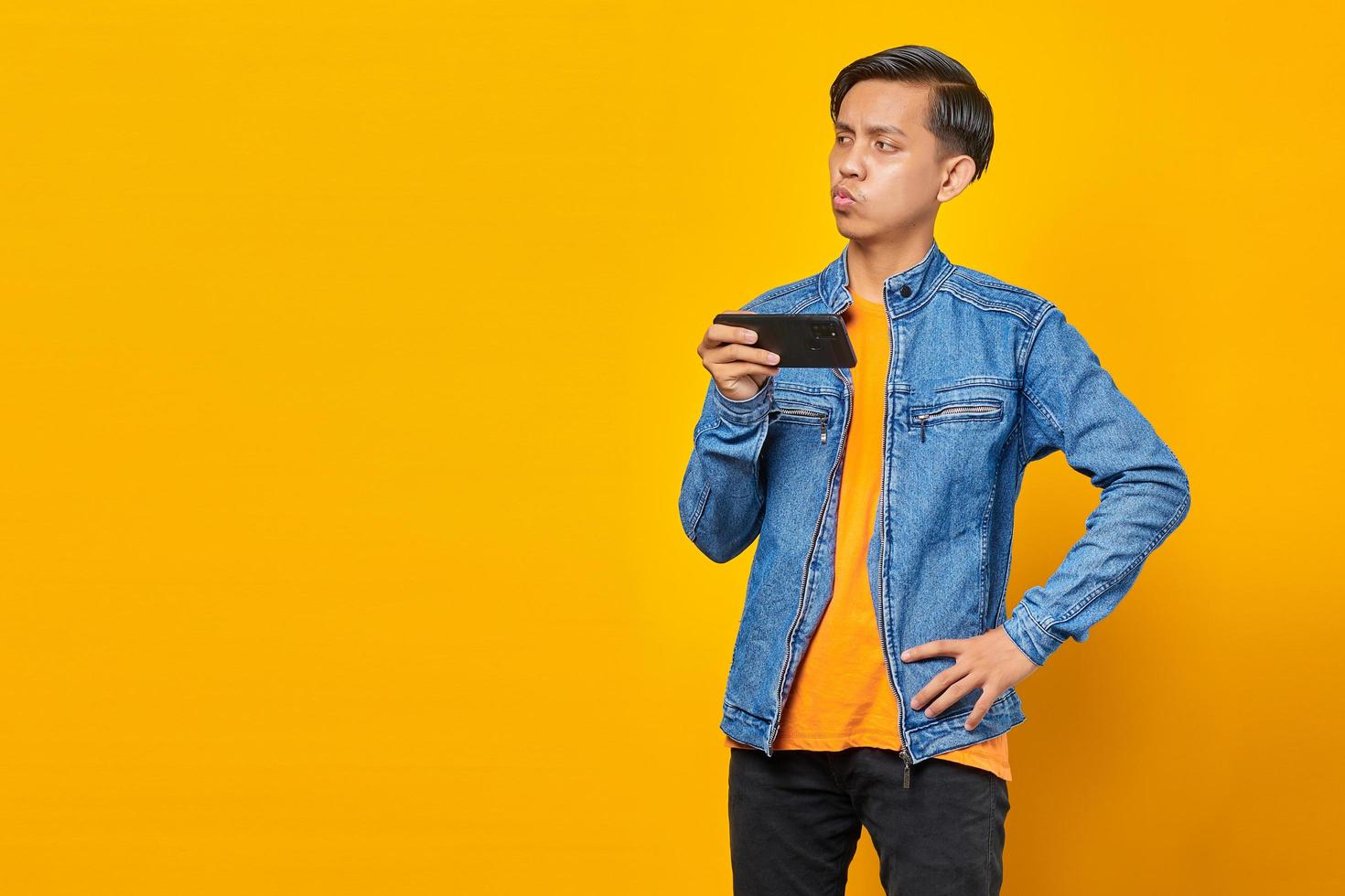 asiatischer Mann mit Handy, der Spiel mit wütendem Gesicht über gelbem Hintergrund spielt foto