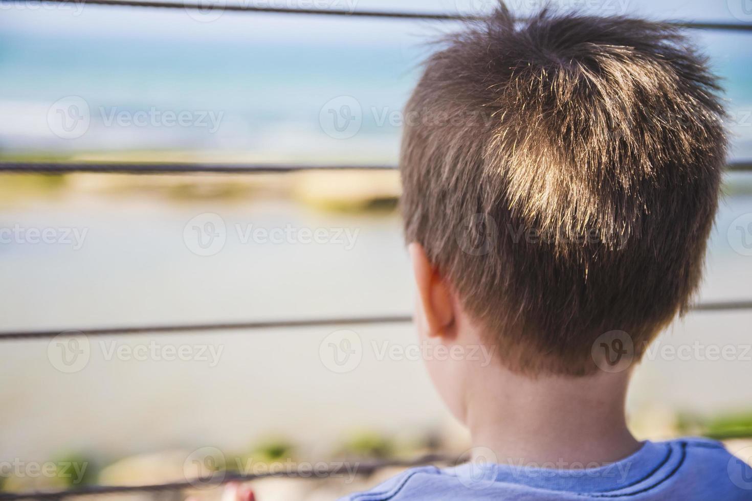 kleiner Junge schaut hinter Metallzaun weit zum Horizont foto