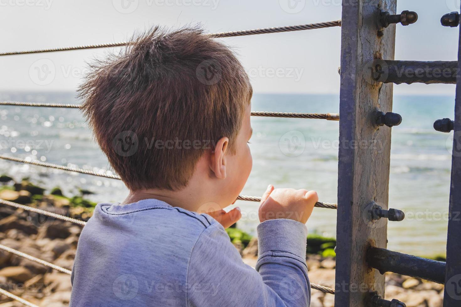 kleiner Junge schaut hinter Metallzaun weit zum Horizont foto