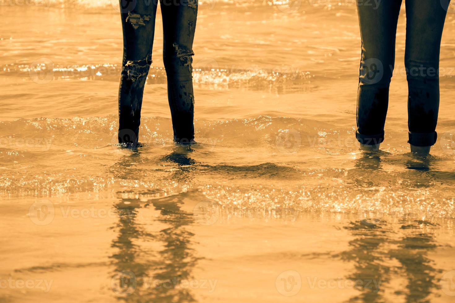 Frauenbeine in Blue Jeans stehen im Meerwasser an der Küste - goldener Ton foto