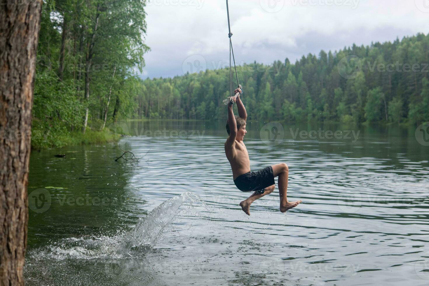 Junge springt in das Wasser mit ein Tarzan schwingen während Schwimmen im ein Wald See foto