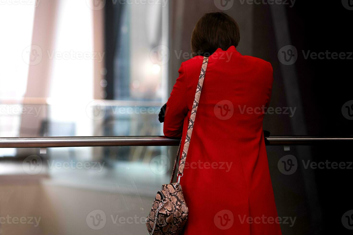 jung Frau im ein rot Mantel steht mit ihr zurück zu das Zuschauer im das Empfangshalle von ein Öffentlichkeit Gebäude foto