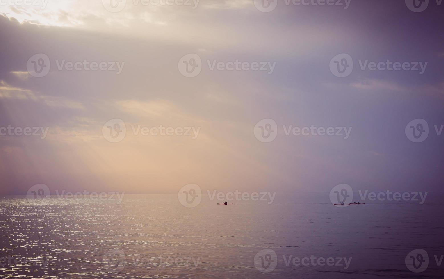 drei Kanus, die bei Sonnenuntergang auf See segeln foto