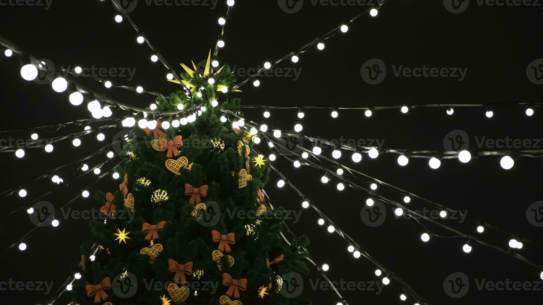 Aussicht von das Unterseite auf das schön Weihnachten Baum mit bunt Dekorationen und Girlande von Weiß Beleuchtung Stehen auf das Quadrat. Konzept. schön schneebedeckt Winter Landschaft von Weihnachten Urlaub foto