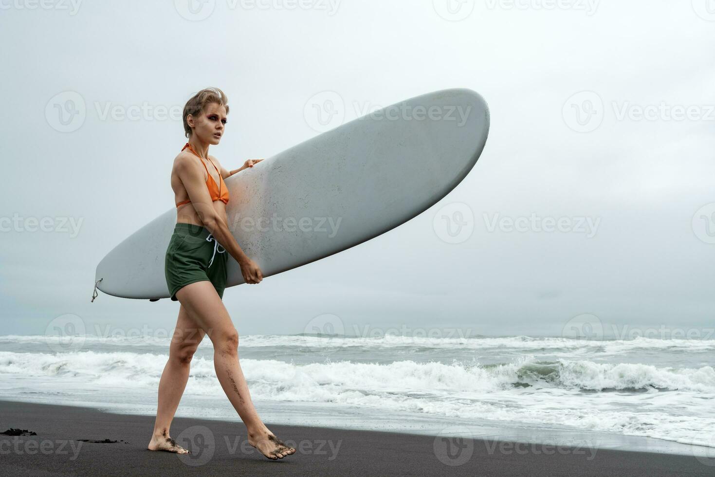 Surfer ist Gehen auf Sand Strand während Sommer- Urlaub, Tragen Surfbrett auf Hintergrund von Meer Wellen foto