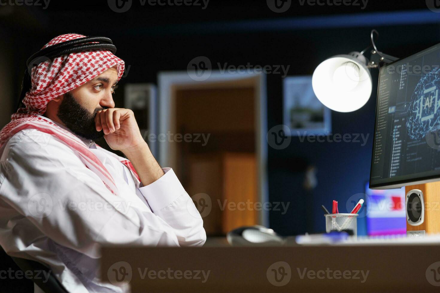 ein arabisch Mann im traditionell Kleidung funktioniert beim ein Computer konzentriert auf Kodierung, stellt sicher Internet-Sicherheit und Monitore das Netzwerk. diese Bild Vitrinen das Integration von Technologie und Kultur. foto