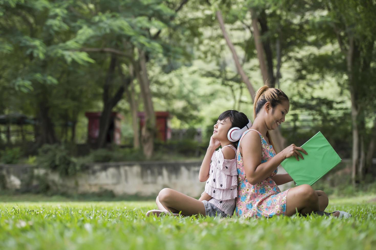 Mutter und Tochter, die ihrer Tochter ein Märchen vorlesen, hören Ton mit Kopfhörer im Park foto