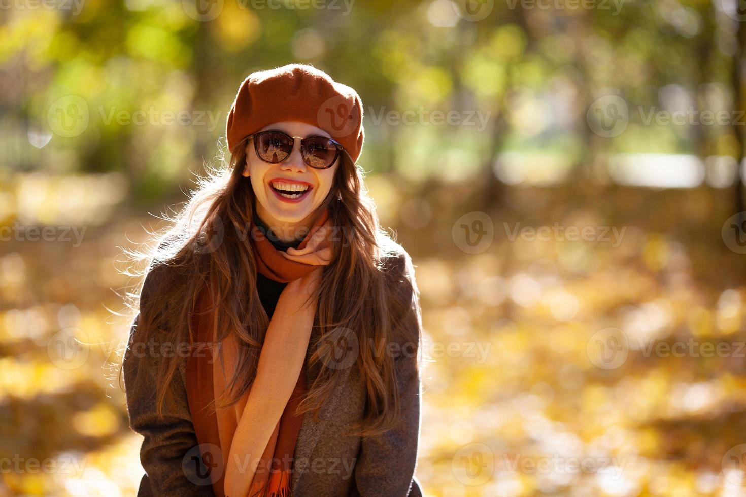 fröhliche junge Frau mit Sonnenbrille und orangefarbenem Barett im Herbstpark foto