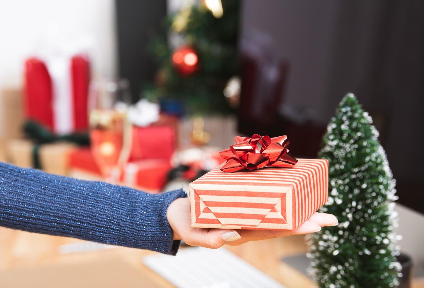 Geschäftsfrau Hand hält Geschenkbox in Weihnachtsferien im Büro mit Weihnachtsdekoration auf dem Tisch. foto