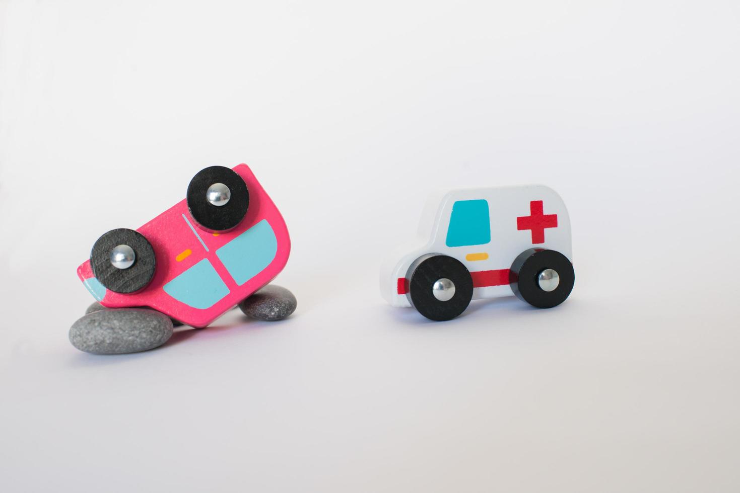 Krankenwagen, der nach einem Autounfall zur Hilfe kommt. Spielzeugautos aus Holz, ein umgekipptes rosa Auto und ein Krankenwagen mit weißem Hintergrund foto