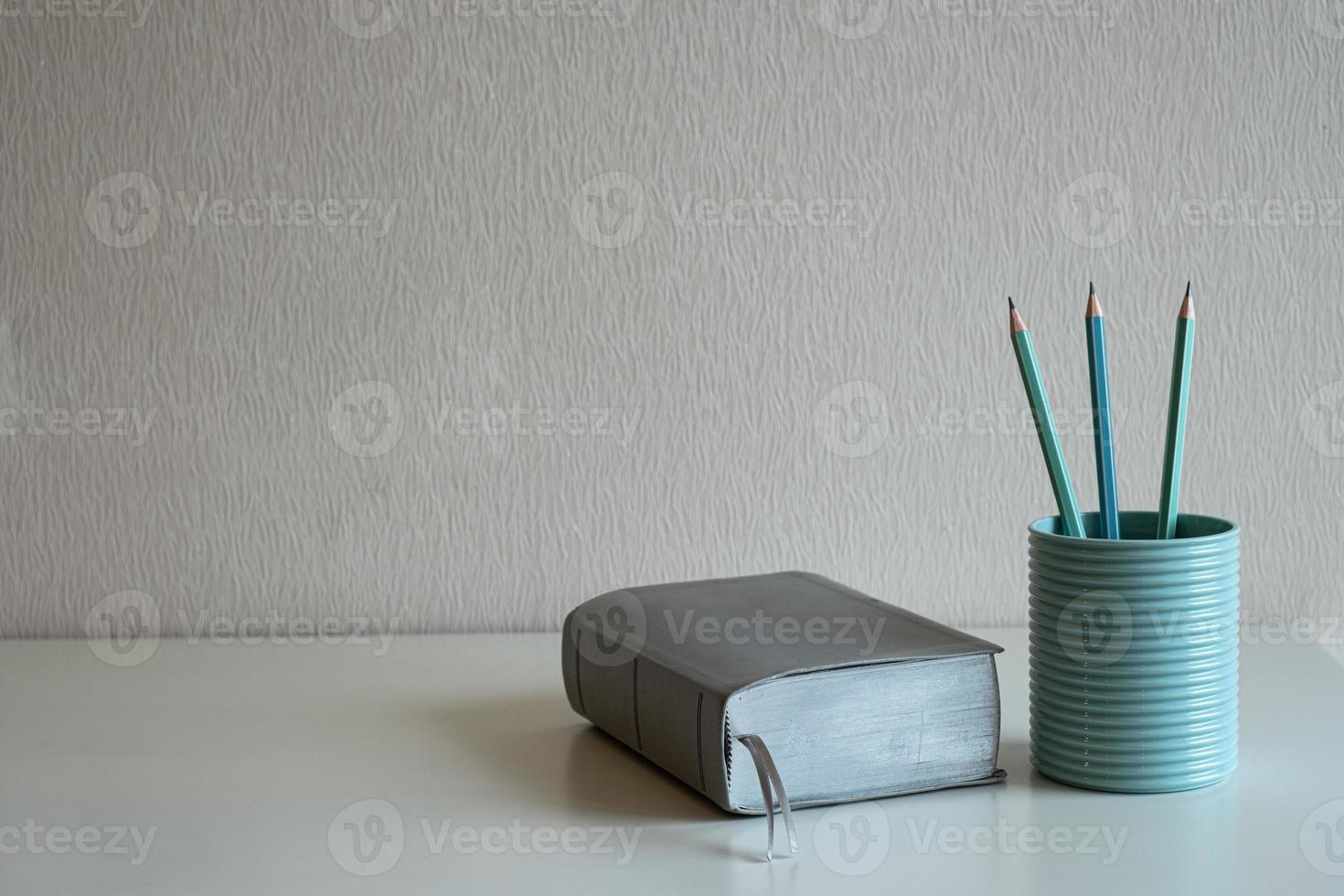 ein Buch und Pastellstifte im blauen Glas auf dem Schreibtisch auf grauem Wandhintergrund foto