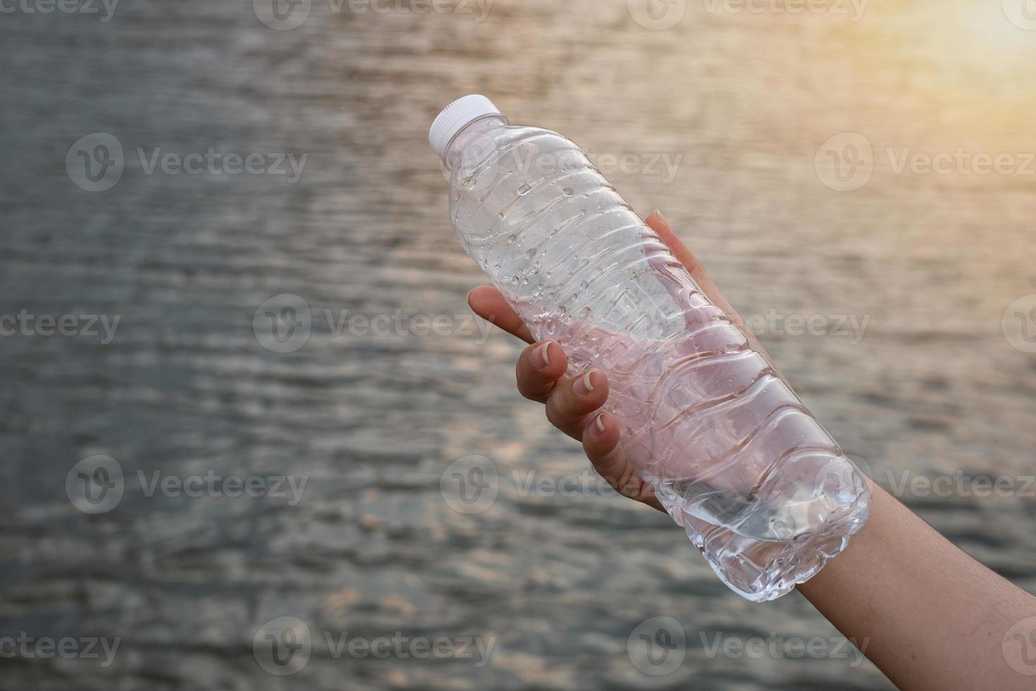 Nahaufnahme der Frau, die die durchsichtige Plastikflasche am Flusshintergrund hält foto