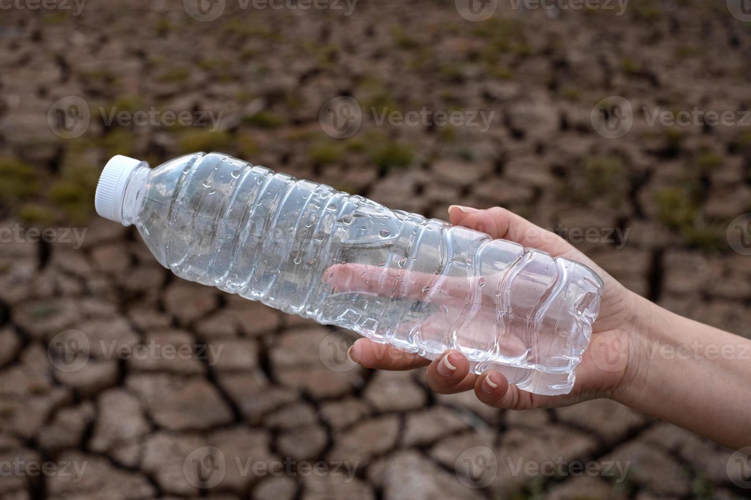 Nahaufnahme der Frauenhand, die die durchsichtige Plastikflasche am Rissbodenhintergrund hält foto